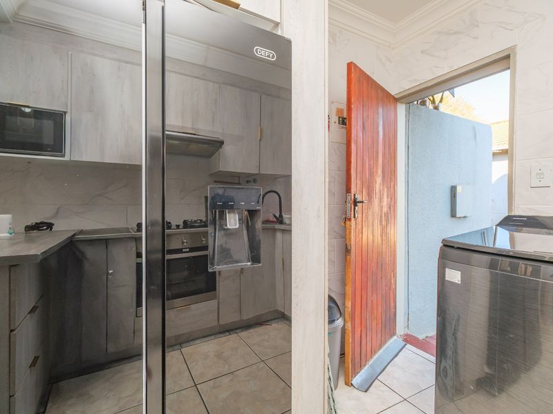 Compact kitchen featuring built-in cabinetry, integrated oven and hob, tiled backsplash, and direct access to an outdoor area.