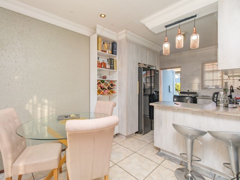 Open-plan kitchen and dining area featuring a breakfast bar, built-in cabinetry, wine storage, and modern pendant lighting with tiled flooring throughout.