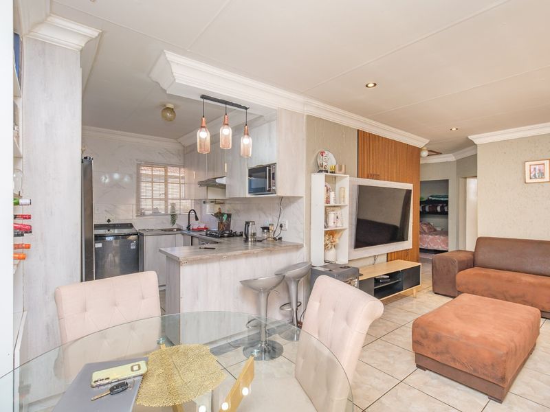 Open-plan living and kitchen area featuring tiled flooring, modern cabinetry, a breakfast bar, and integrated kitchen appliances, creating a functional and connected living space.