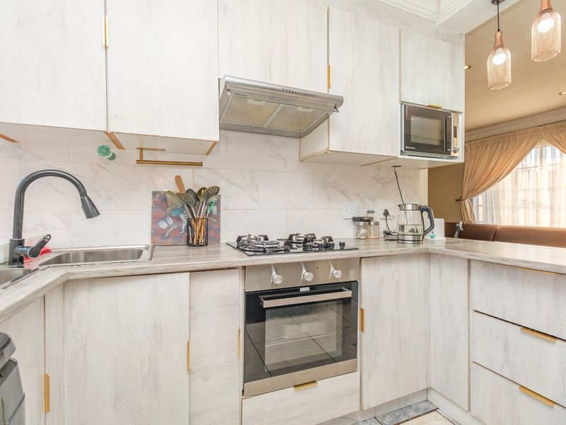 A well-maintained kitchen featuring light wood-grain cabinetry, a gas hob, built-in oven, extractor fan, and modern marble-look backsplash tiling.