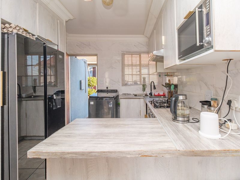 A functional galley-style kitchen featuring light-toned cabinetry, laminate countertops, a gas hob, and an integrated microwave, with direct access to an outdoor utility area.