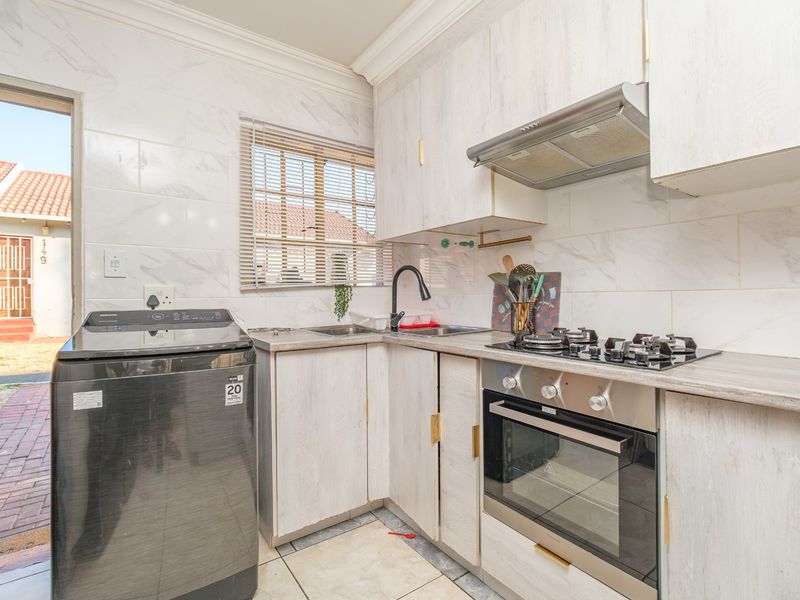 Compact kitchen featuring light wood-look cabinetry, gas hob, built-in oven, extractor fan, and marble-effect wall tiling with direct access to the exterior.