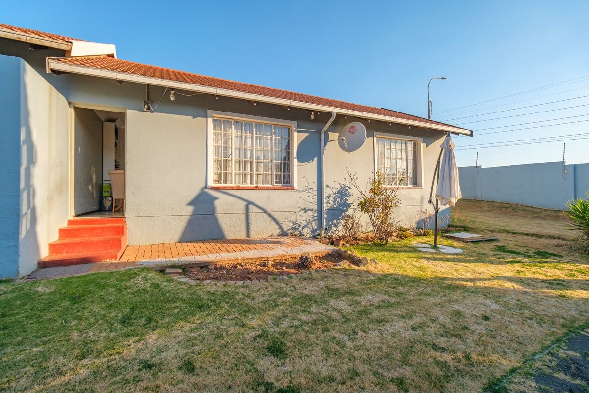 Rear exterior view of the townhouse featuring a tiled roof, brick patio area, and a private garden enclosed by a perimeter wall with electric fencing.