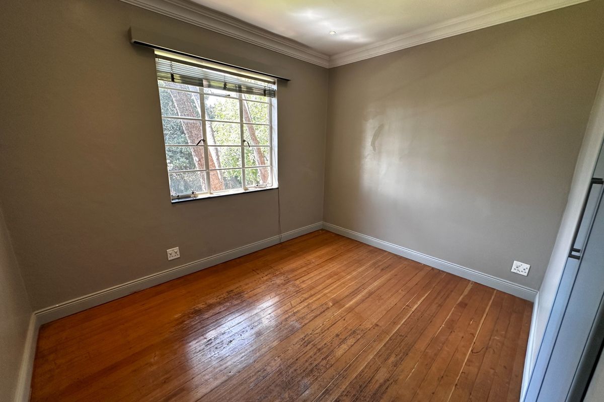 An empty bedroom featuring original timber flooring, neutral wall paint, and a window with security bars.