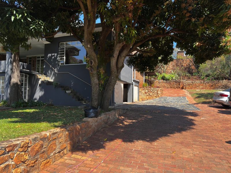 Front exterior view of the property featuring a brick driveway, stone retaining wall, and an external staircase leading to the entrance.
