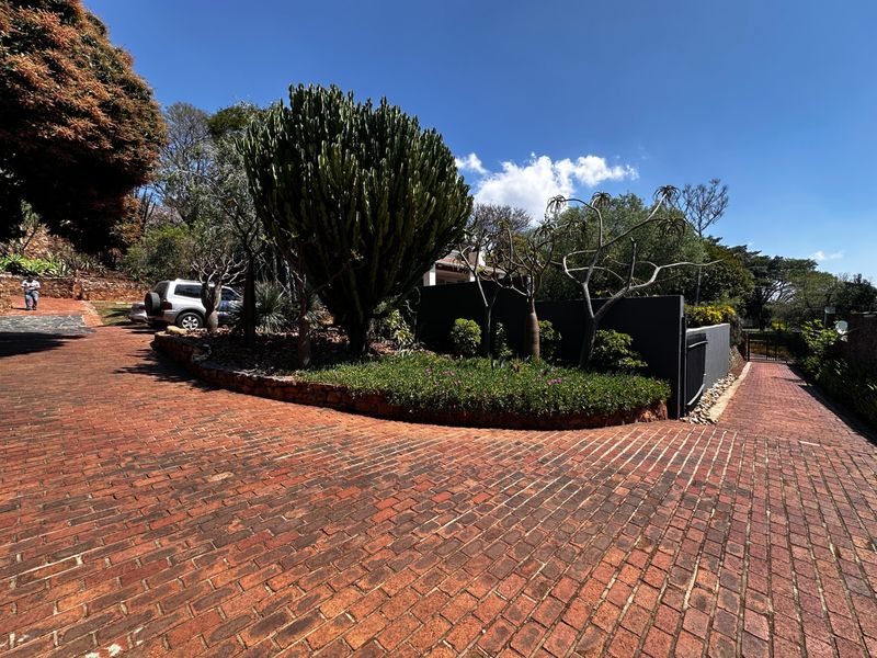 A well-maintained brick paved driveway leading to the property entrance, featuring established garden beds and a retaining wall.