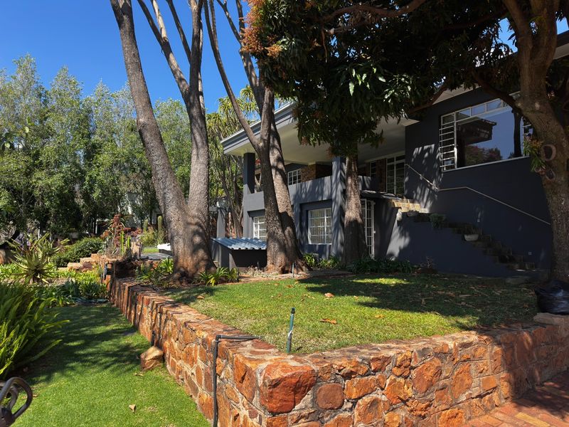 Rear view of the property featuring a stone retaining wall, landscaped garden, and a covered patio area with an external staircase.