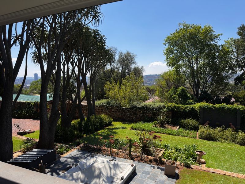A well-maintained garden featuring a slate patio, stone retaining wall, and mature trees with a scenic view of the surrounding area.