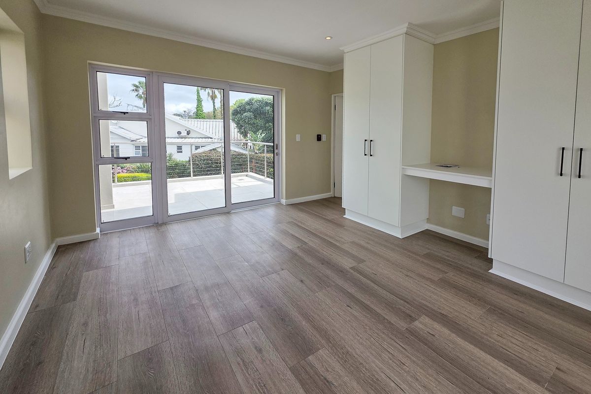 Bright and spacious bedroom featuring modern laminate flooring, built-in cupboards with an integrated desk, and sliding doors leading to an outdoor balcony.