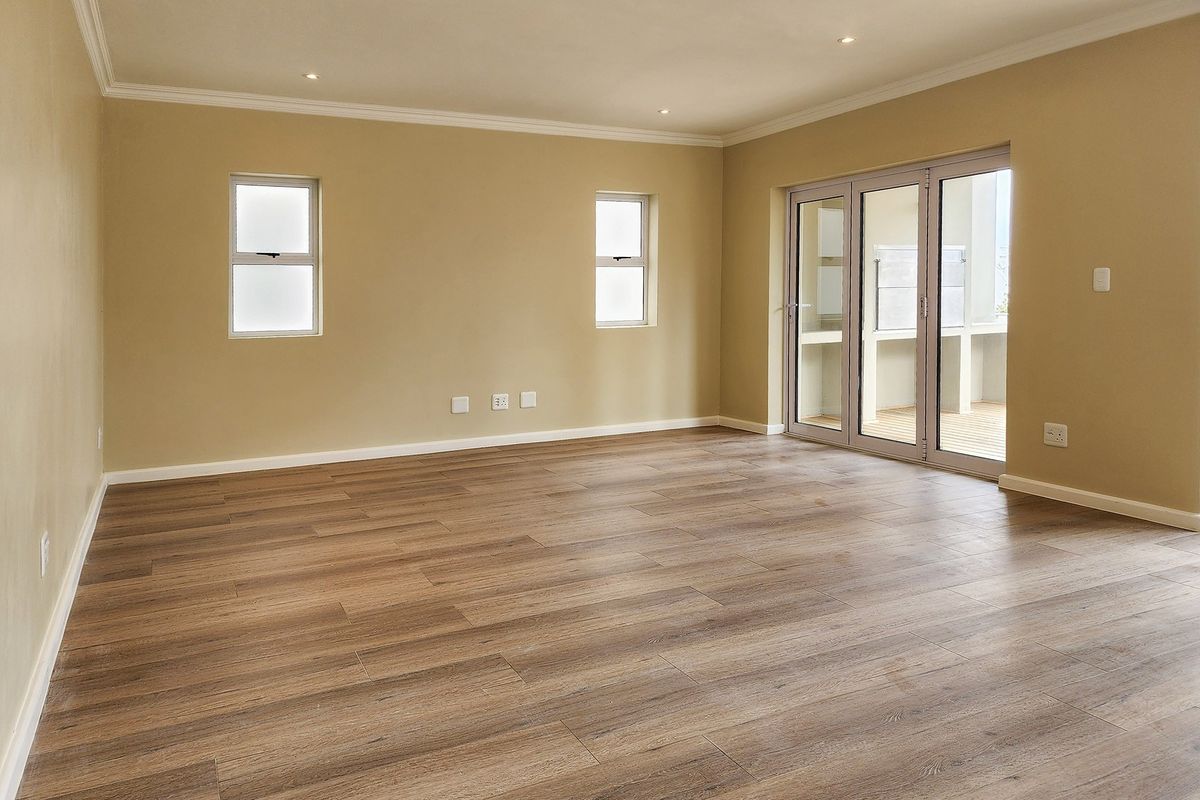 Spacious, empty living area featuring modern laminate flooring, recessed downlights, and large sliding glass doors leading to an outdoor patio.