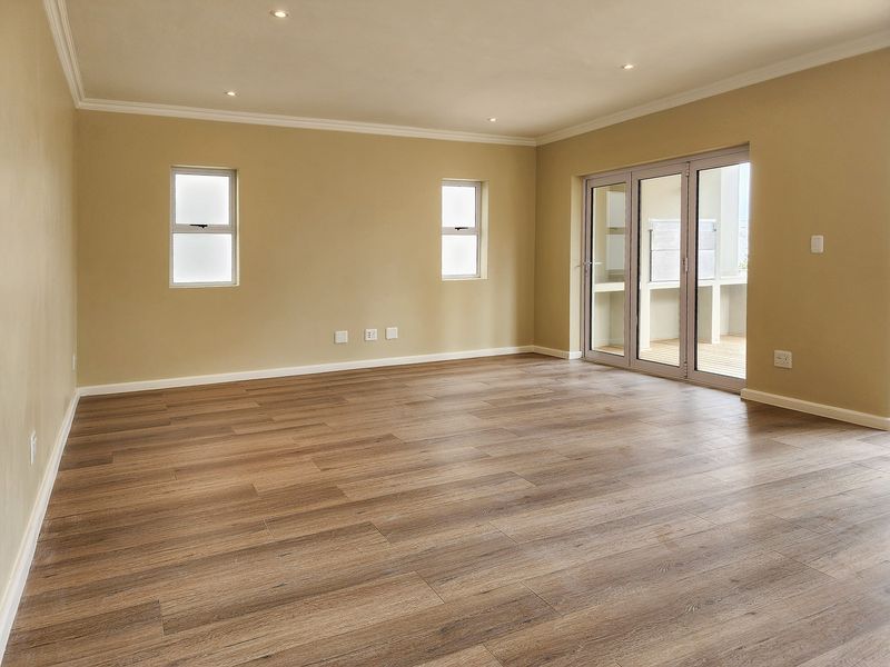 Spacious, empty living area featuring modern laminate flooring, recessed downlights, and large sliding glass doors leading to an outdoor patio.