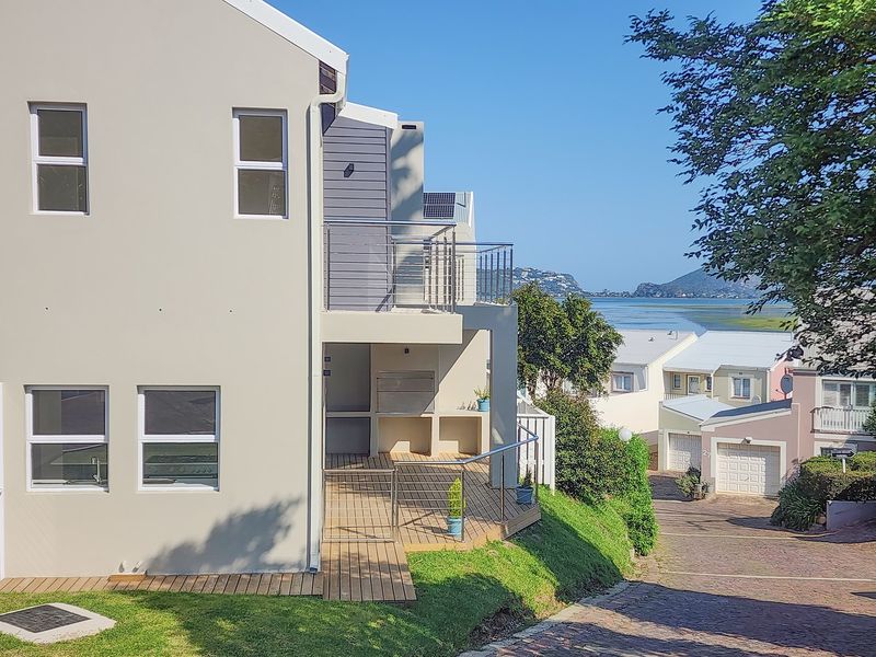 Rear view of the property featuring a timber deck, built-in braai area, and stainless steel balustrades with scenic water views.