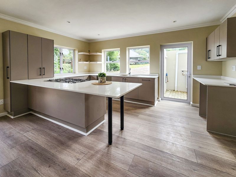 Modern kitchen featuring sleek cabinetry, stone countertops, a central island with a gas cooktop, and wood-look laminate flooring with direct outdoor access.