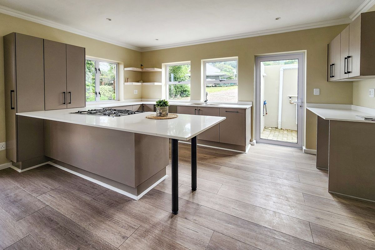 Modern kitchen featuring sleek cabinetry, stone countertops, a central island with a gas cooktop, and wood-look laminate flooring with direct outdoor access.