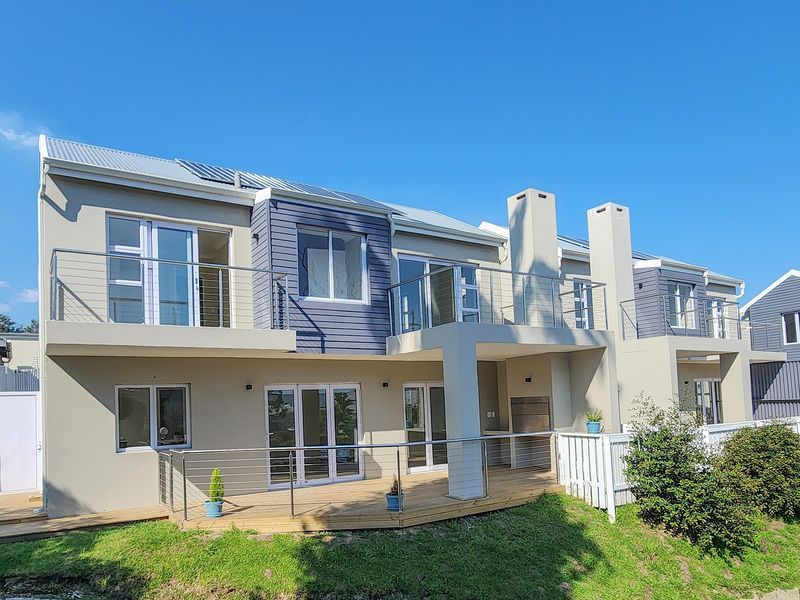 Rear elevation of a modern double-story townhouse featuring timber decking, stainless steel balustrades, built-in braai, and solar water heating panels.