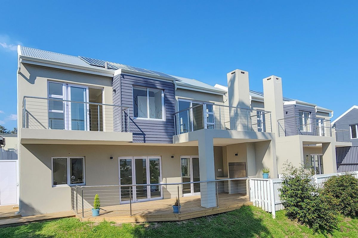 Rear elevation of a modern double-story townhouse featuring timber decking, stainless steel balustrades, built-in braai, and solar water heating panels.
