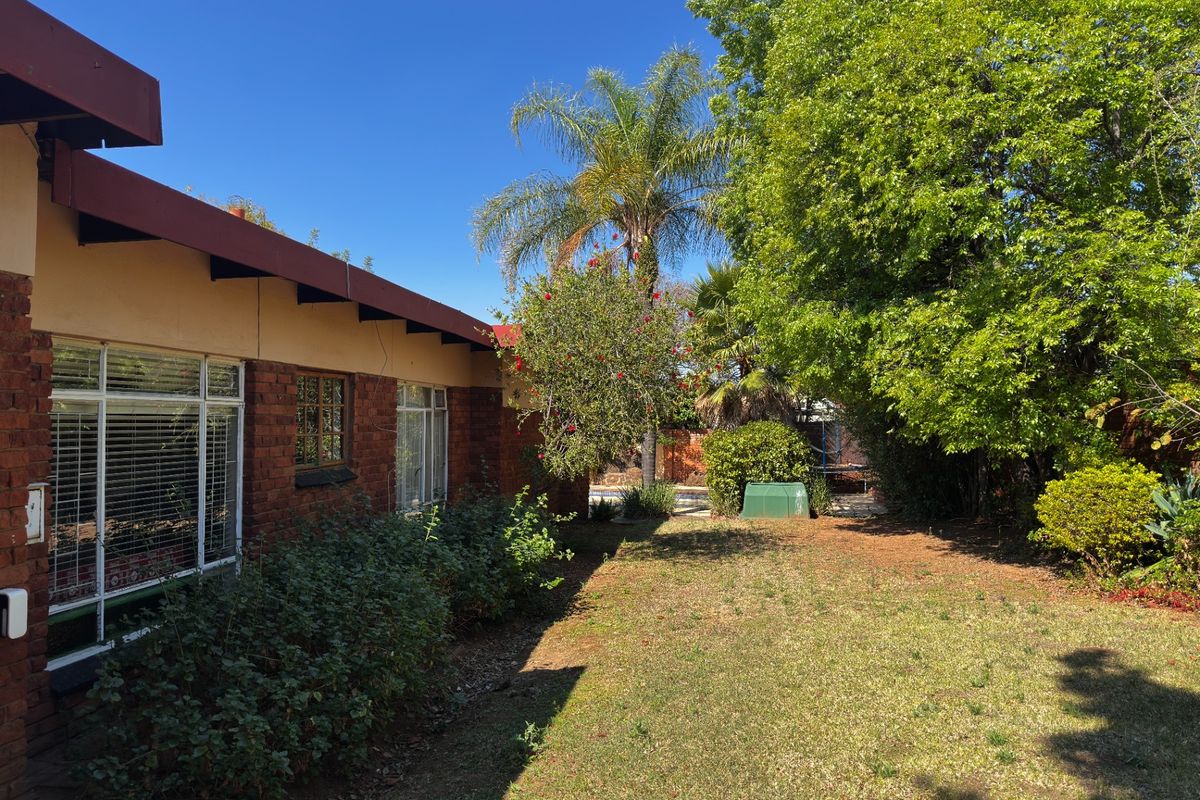 A view of the rear brick facade and garden area, featuring mature trees and established landscaping.