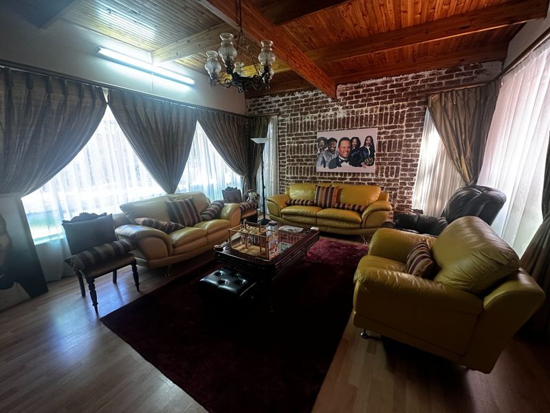 Spacious living room featuring a rustic exposed brick wall, high timber beam ceilings, and laminate flooring, creating a warm and character-filled atmosphere.