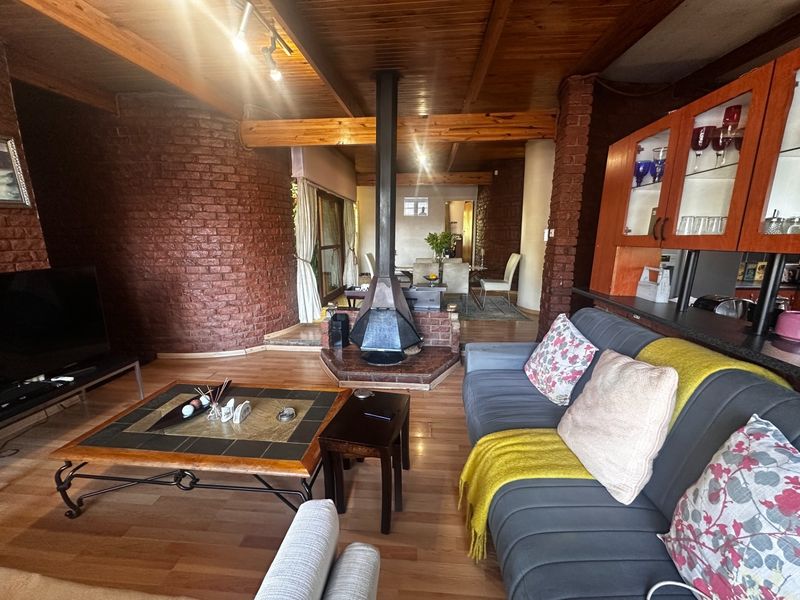 Open-plan living area featuring exposed brick walls, timber ceiling beams, and a central freestanding fireplace, creating a rustic and warm atmosphere.