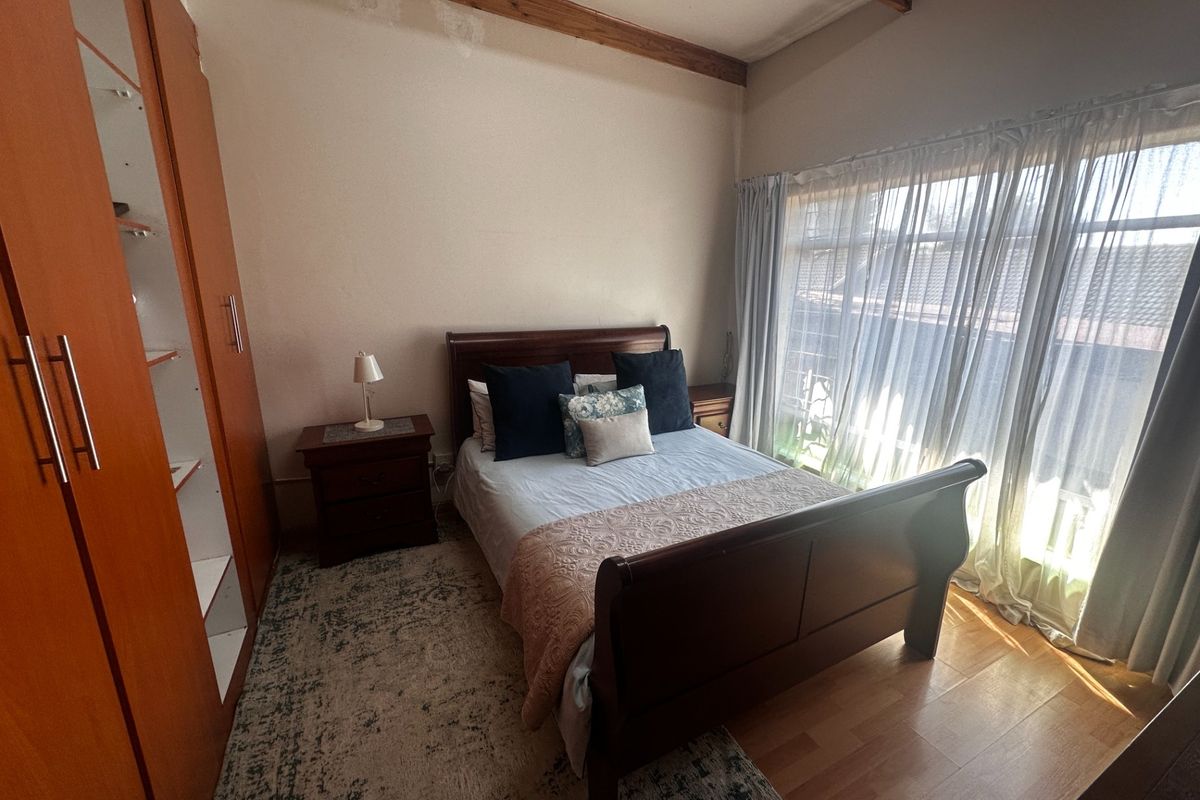 Bedroom featuring laminate flooring, exposed timber ceiling beams, and a built-in wardrobe, with visible ceiling water staining.