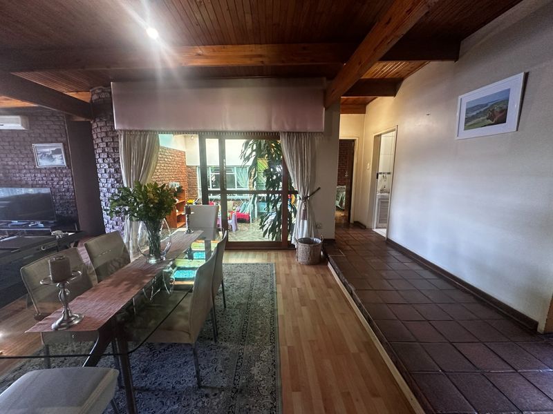 Spacious living area featuring exposed timber beam ceilings, a brick feature wall, and a seamless transition between laminate and tiled flooring.