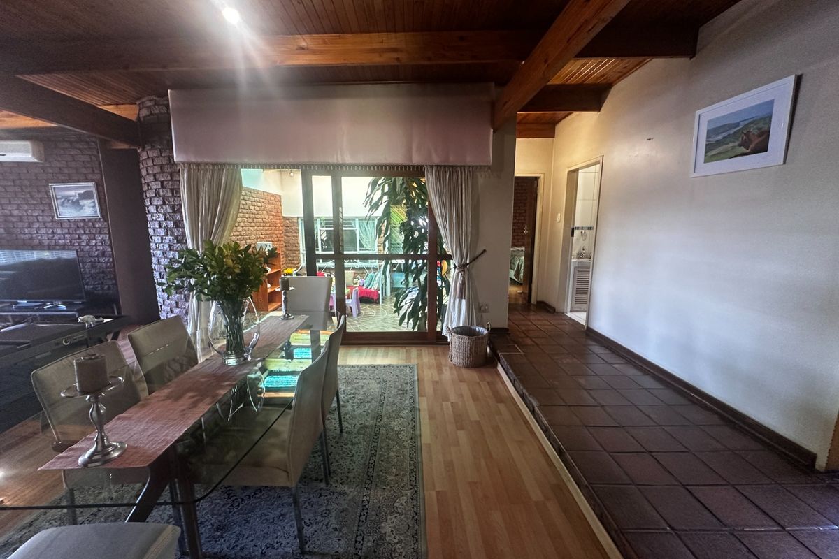 Spacious living area featuring exposed timber beam ceilings, a brick feature wall, and a seamless transition between laminate and tiled flooring.