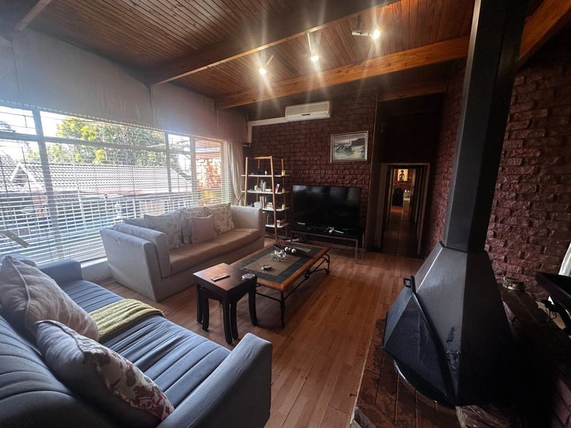 Cozy living room featuring exposed brick walls, timber beam ceilings, a freestanding fireplace, and large windows providing ample natural light.