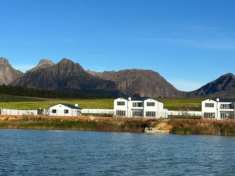 A scenic view of the rear elevation of the property featuring white multi-story buildings situated along a lake with mountain views.