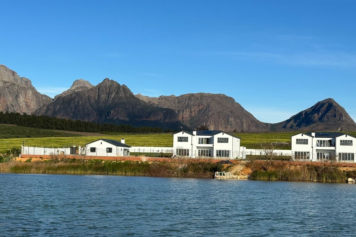 A scenic view of the rear elevation of the property featuring white multi-story buildings situated along a lake with mountain views.