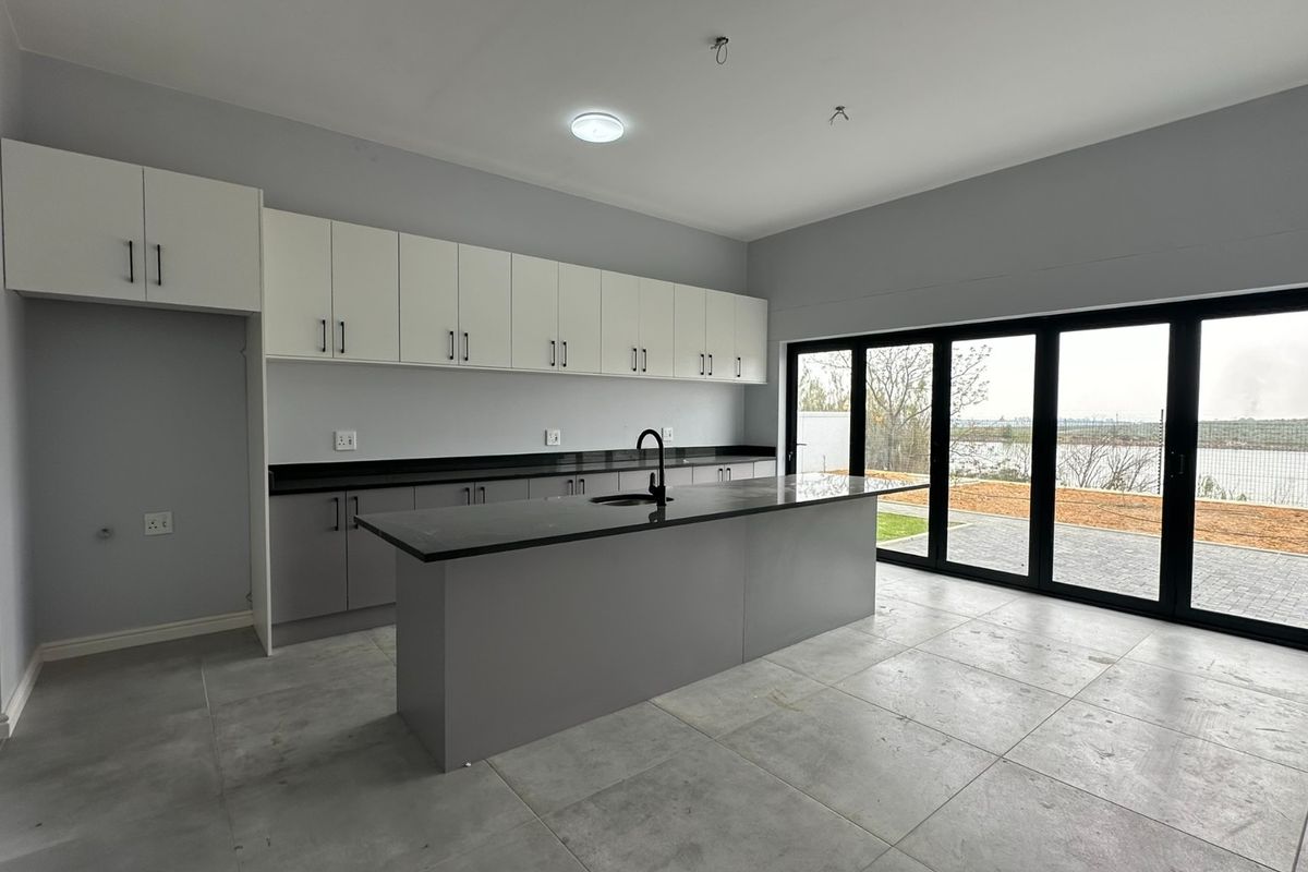 Modern kitchen featuring a central island, sleek cabinetry, stone countertops, and large bi-fold doors opening to an outdoor area.