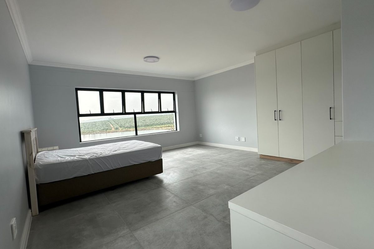 Spacious bedroom featuring large windows with scenic views, neutral tiled flooring, and ample built-in cupboard storage.