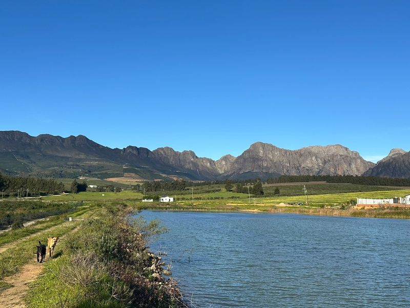 A scenic landscape view featuring a tranquil dam with expansive mountain ranges in the background under a clear blue sky.