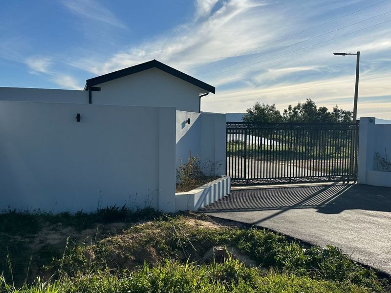 Front entrance view featuring a modern perimeter wall, secure metal driveway gate, and exterior lighting.