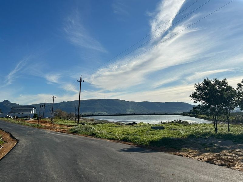 A scenic view of a local road leading towards a lake with mountain vistas in the background under a clear blue sky.