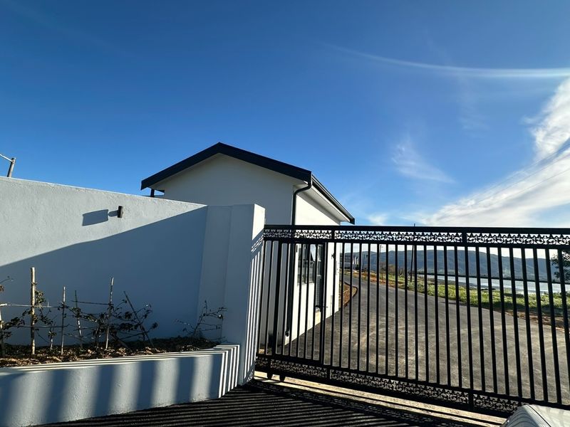 A modern property entrance featuring a secure sliding gate, perimeter wall, and paved driveway with clear views of the surrounding landscape.
