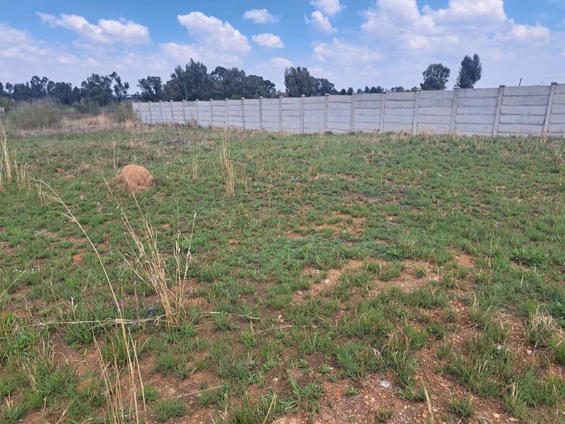 A vacant residential plot featuring natural grass coverage and a secure precast concrete boundary wall along the rear perimeter.