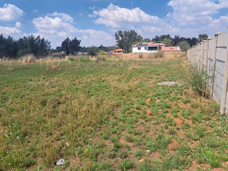 A view of a vacant residential plot featuring natural grass cover and a precast concrete boundary wall along the side perimeter.