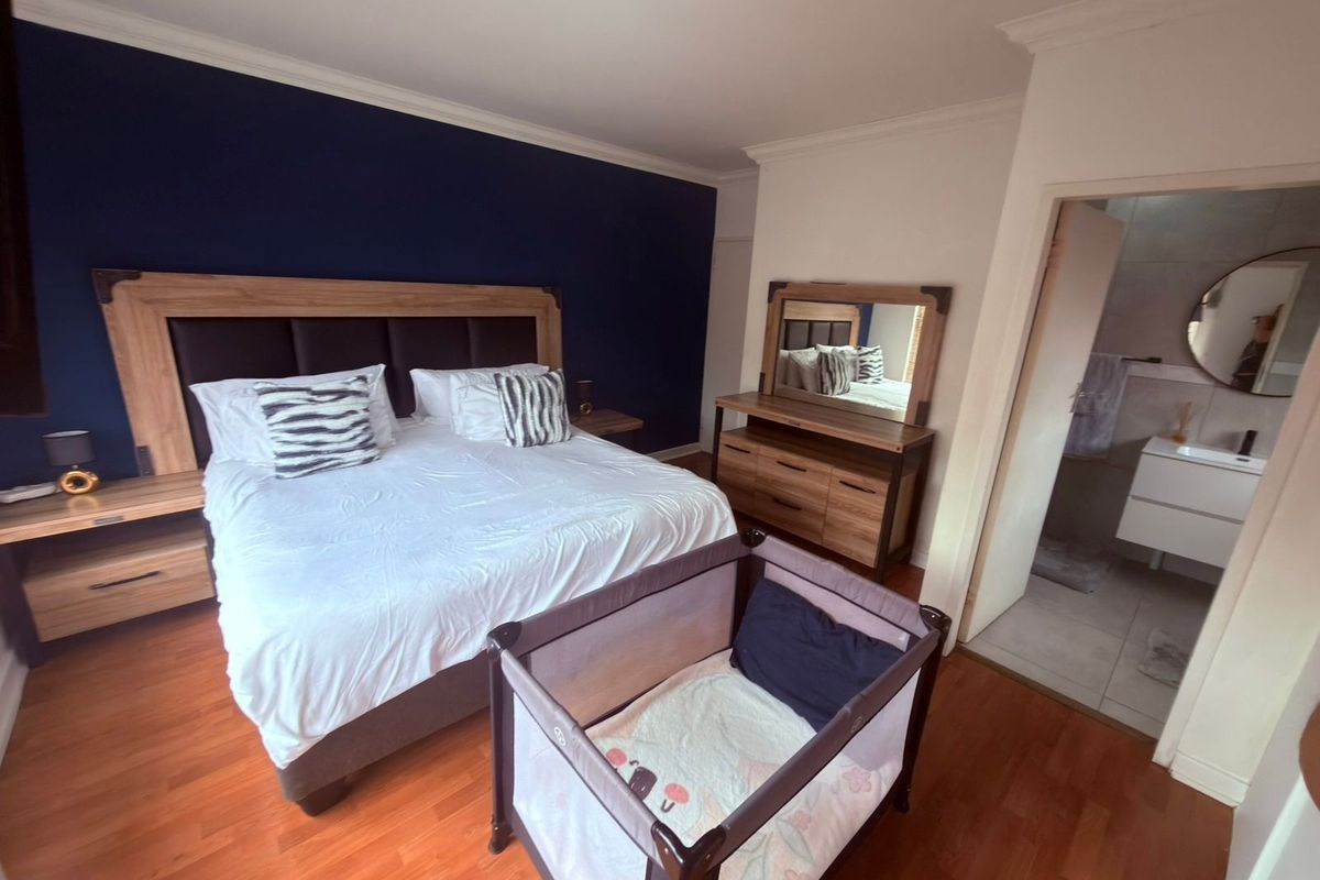 Spacious bedroom featuring laminate flooring, a dark accent wall, and direct access to an en-suite bathroom with modern vanity.