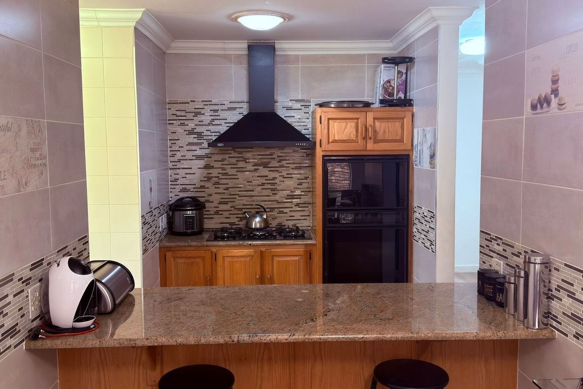 A functional kitchen featuring wooden cabinetry, granite countertops, a built-in oven, and a gas hob with a modern extractor fan.