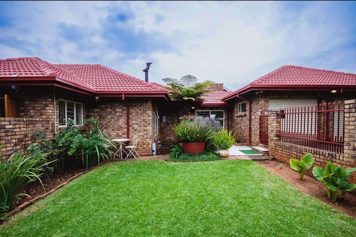 A well-maintained rear garden area featuring a face brick facade, tiled roof, and a neat lawn with paved access.