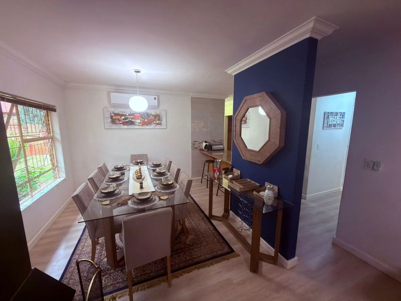 A well-maintained dining room featuring laminate flooring, cove cornicing, and a wall-mounted split-system air conditioner, providing a comfortable space for formal meals.