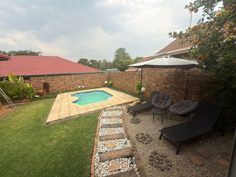 Private backyard featuring a small swimming pool, paved surround, gravel seating area, and established brick boundary walls.