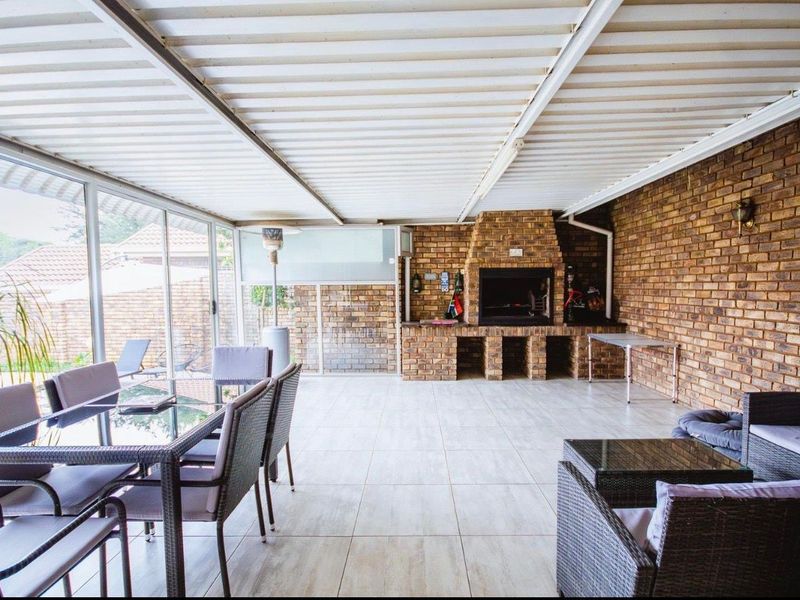 Spacious covered patio featuring a built-in brick braai, tiled flooring, and large sliding glass doors, ideal for outdoor entertaining.