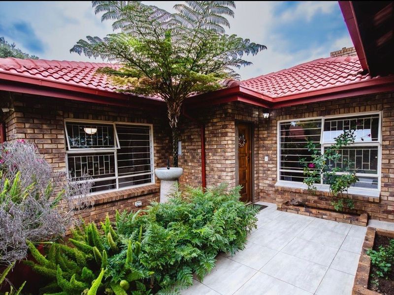 A well-maintained face brick entrance featuring a tiled patio, secure window bars, and a classic timber front door under a tiled roof.