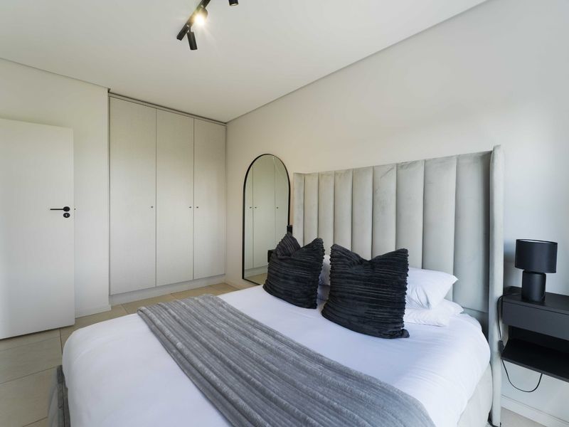 A modern, well-maintained bedroom featuring neutral tones, built-in cupboards, and contemporary track lighting.