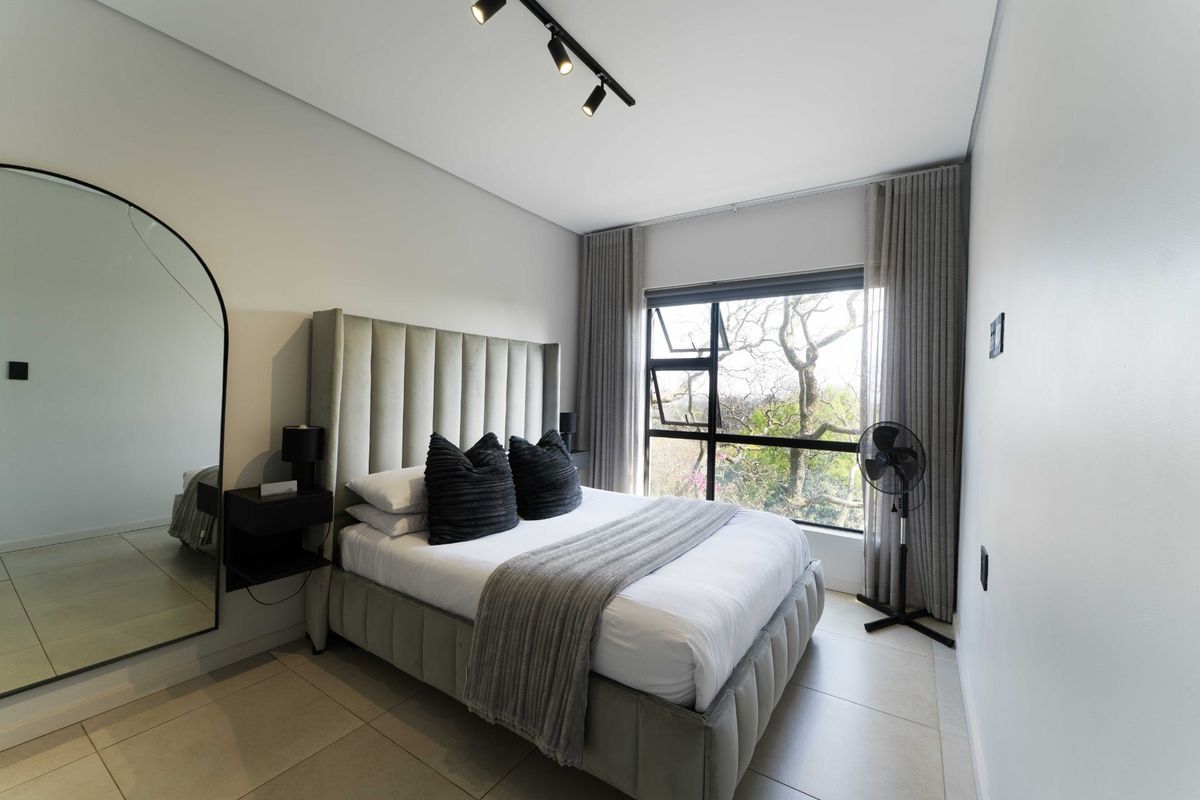 A modern, well-maintained bedroom featuring neutral tiled flooring, contemporary track lighting, and large windows with integrated curtain tracks.