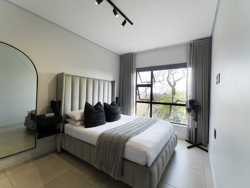 A modern, well-maintained bedroom featuring neutral tiled flooring, contemporary track lighting, and large windows with integrated curtain tracks.