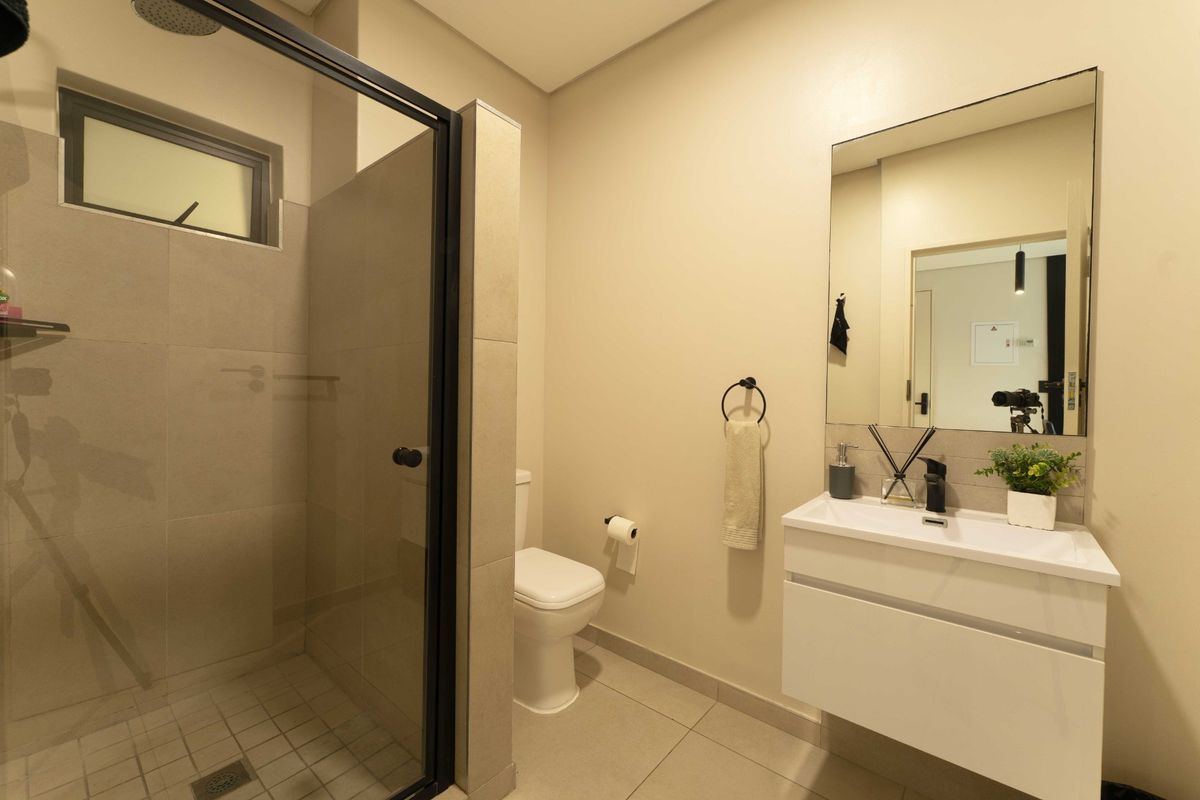 Modern bathroom featuring a walk-in shower with black-framed glass, a sleek wall-mounted vanity with basin, and neutral floor-to-ceiling tiling.