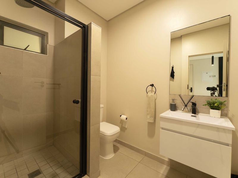 Modern bathroom featuring a walk-in shower with black-framed glass, a sleek wall-mounted vanity with basin, and neutral floor-to-ceiling tiling.