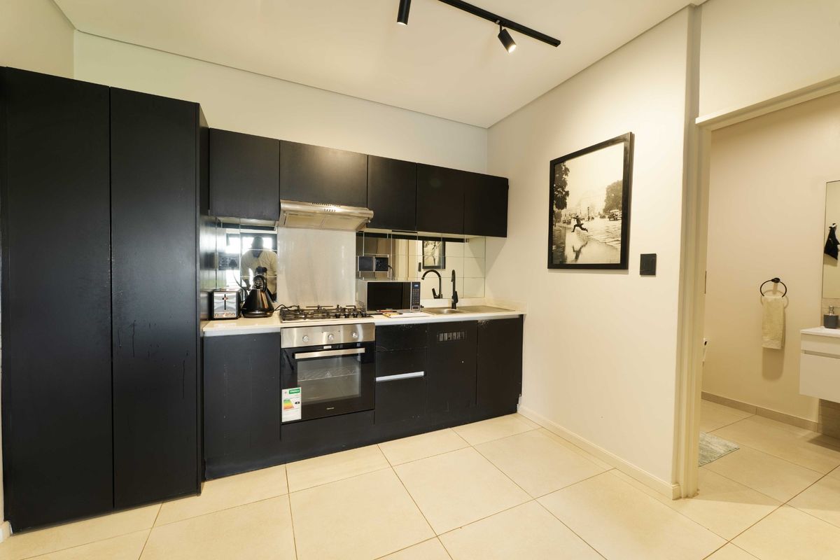 Modern kitchen featuring sleek black cabinetry, integrated gas hob, electric oven, extractor fan, and a mirrored splashback, complemented by neutral tiled flooring.